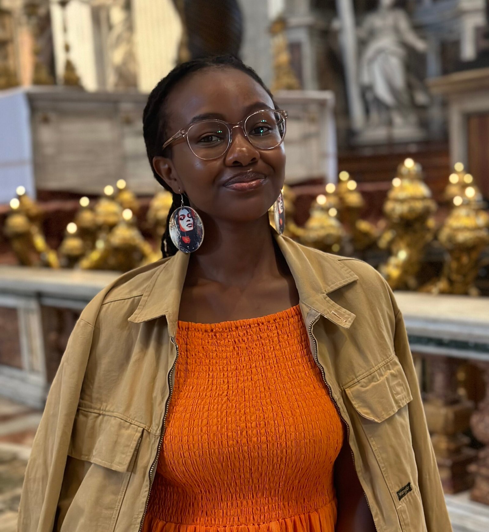 Photo of the author Becky at the Vatican. Wearing an orange dress with yellow mustard jacket, and colorful earrings