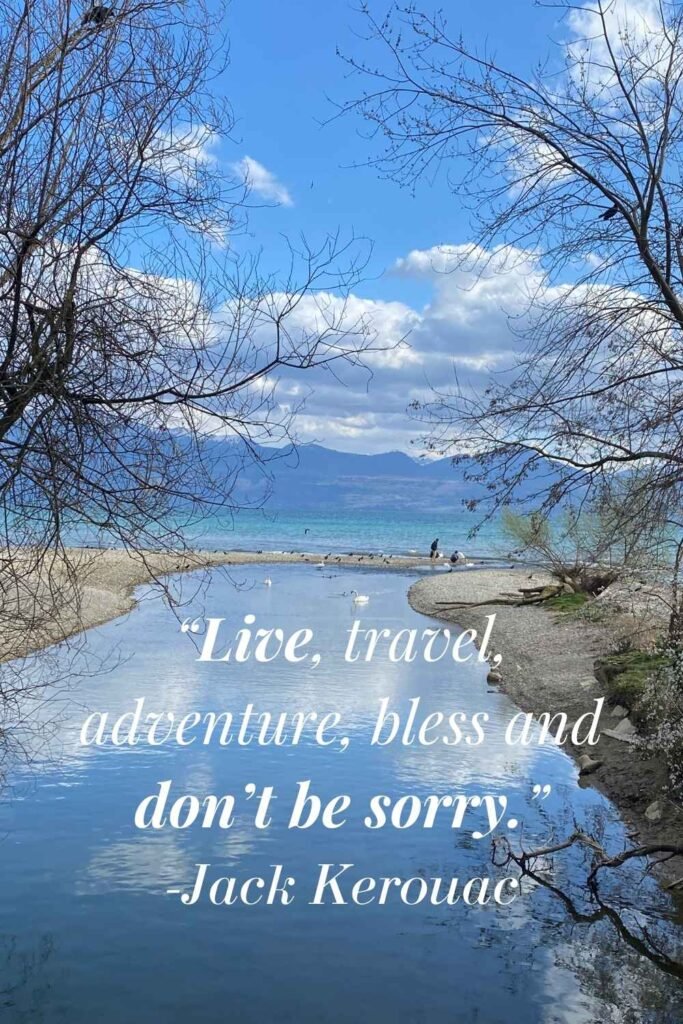 Inspirational travel quote ‘Live, travel, adventure, bless and don’t be sorry – Jack Kerouac’ over a scenic photo of a Swiss river flowing to the ocean with mountains in the background.
