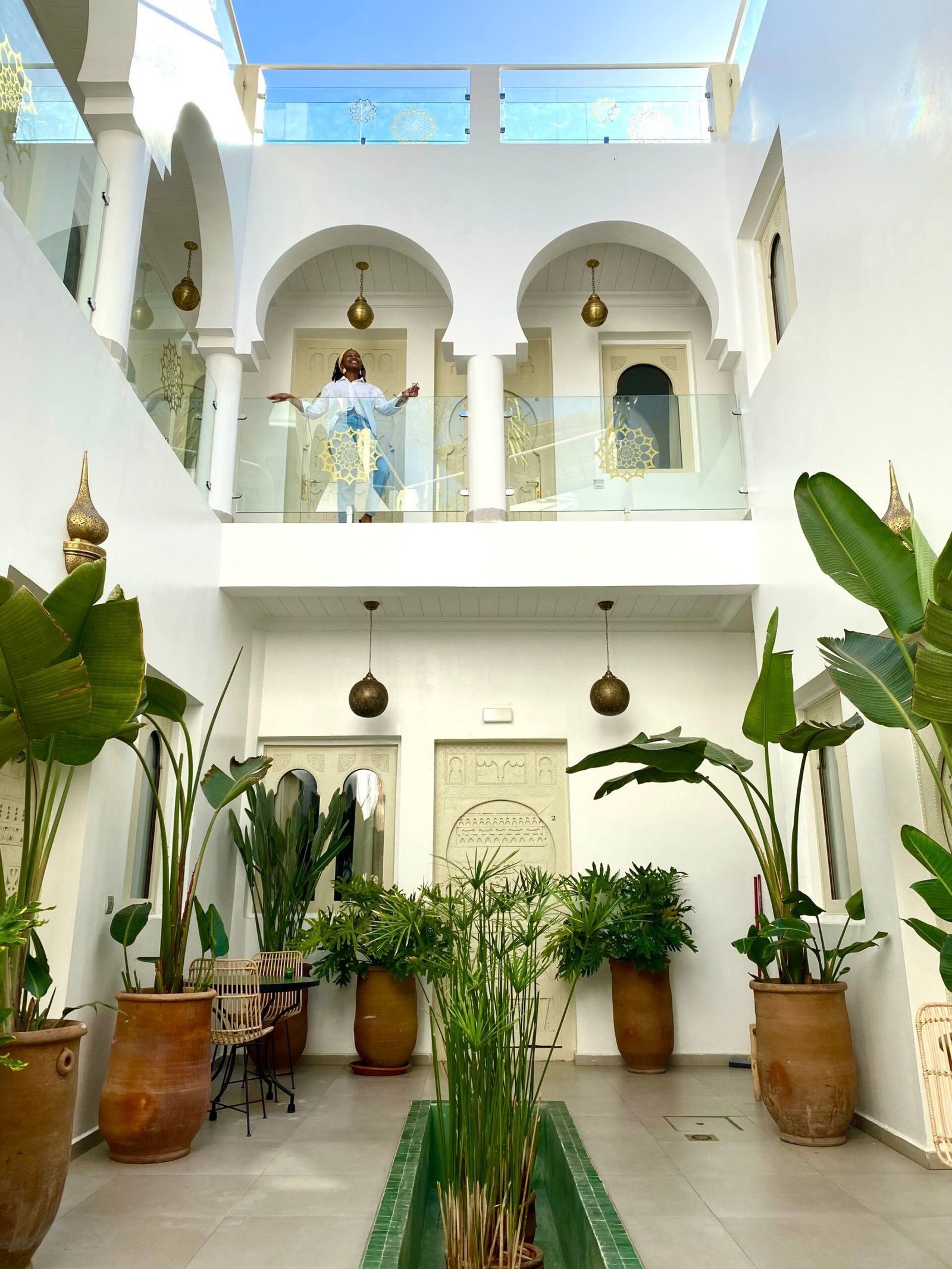 White lobby of a riad in Marrakech, Morocco - filled with plants and white lamps and a person posing on the top floor