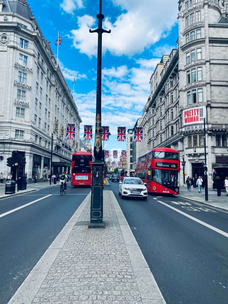 Street in west end area of london, uk with two red buses visible, cyclists, pedestrians and uk flag
