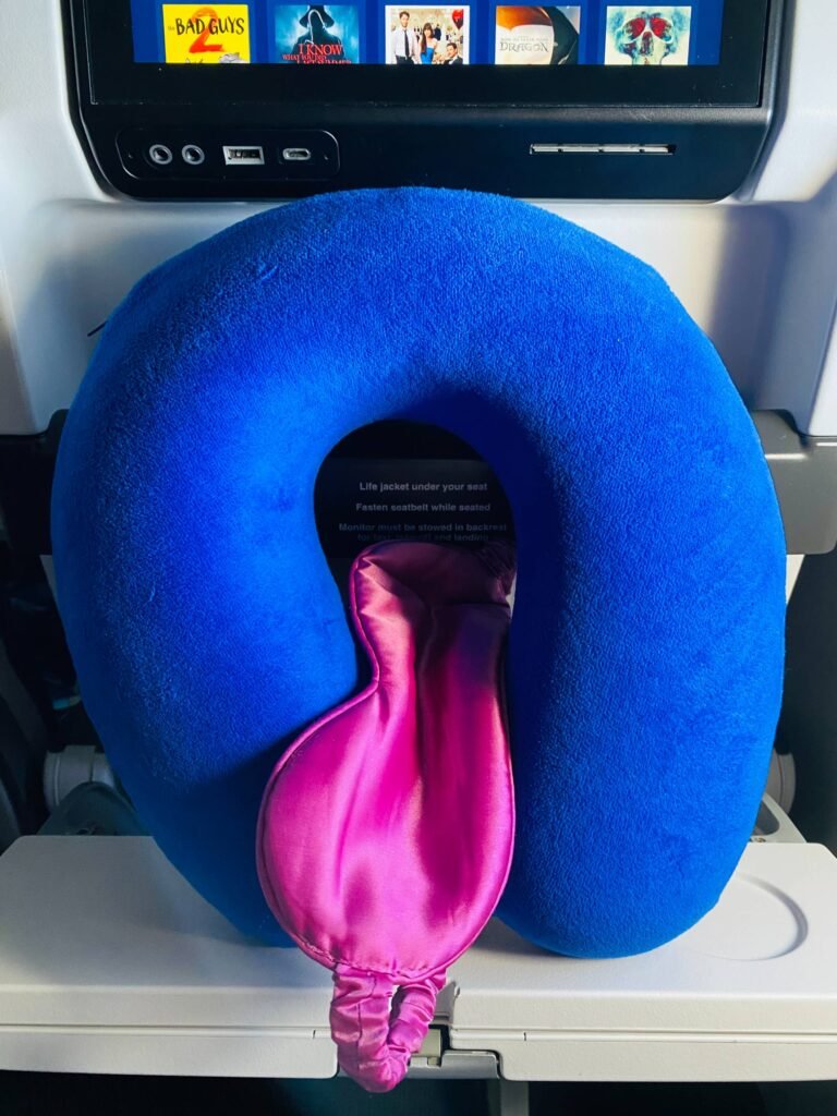 Blue neck pillow and pink eye mask pictured on airport tray table