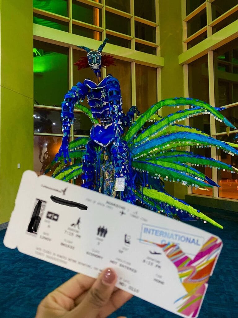 passenger holding boarding pass in front of carnival decoration at port of spain airport in trinidad and tobago
