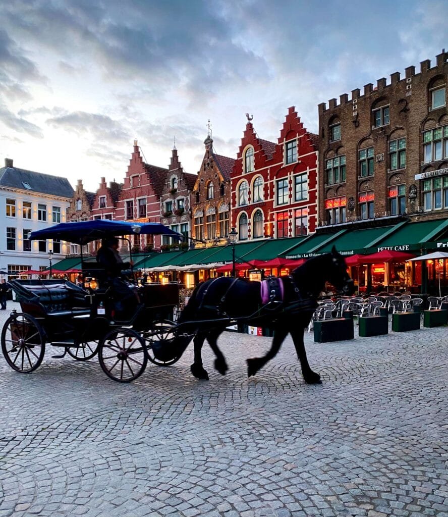 Horse-driven carriage passing in-front of a row of colourful ornate buildings in Bruges, Belgium on a autumn evening