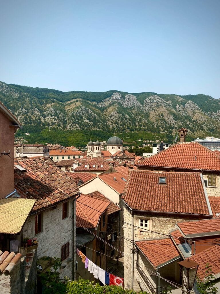 Red-tiled rooftops in Kotor’s old town with a church tower rising above them and mountains in the background.