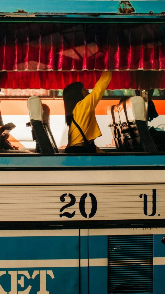 A woman adjusting a curtain inside a vintage public bus during the day.
