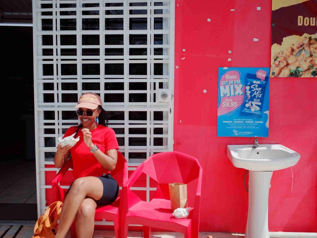 woman sitting outside a caribbean stall eating doubles, a popular cuisine in tobago