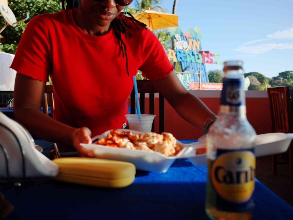 a woman in a red short enjoying some food and drink at anchor bar and grill in tobago