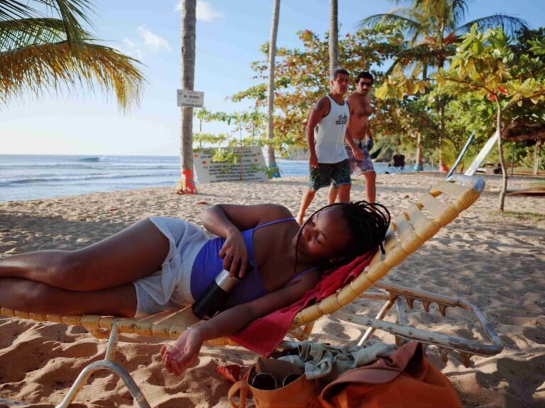 woman in swim clothes lounging in beach with two men walking by