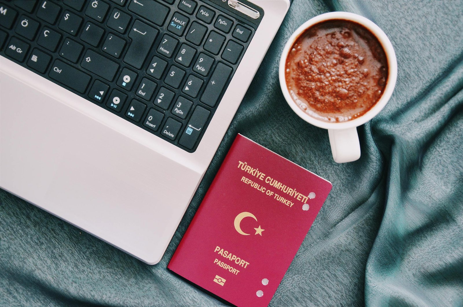 A passport beside a coffee cup and laptop, symbolizing travel preparation and planning