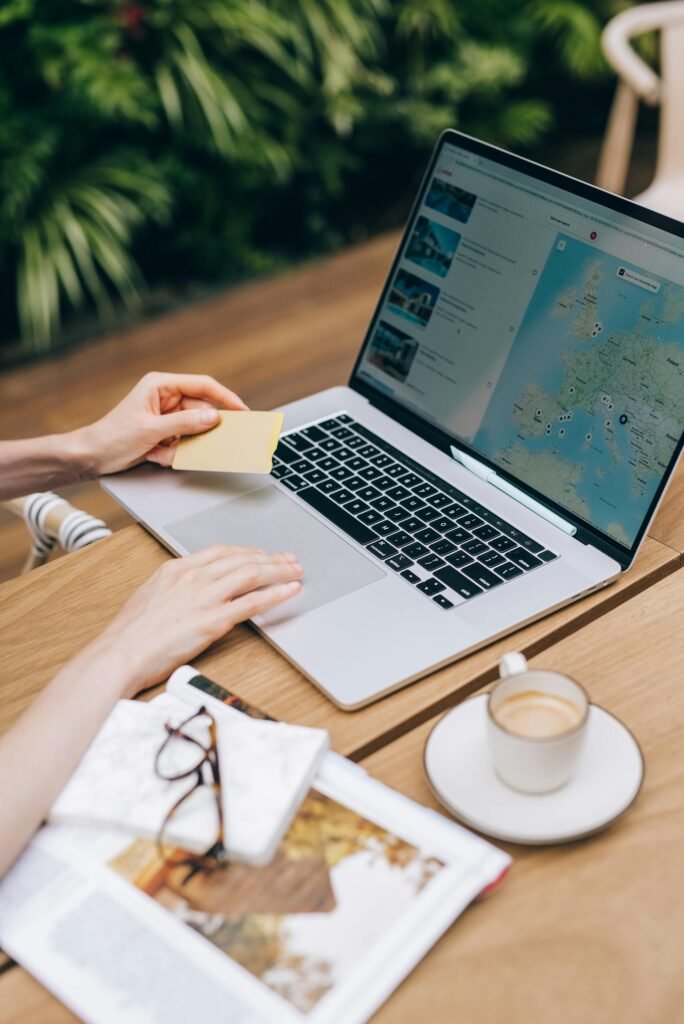 A person using a laptop and credit card, surrounded by a magazine and coffee cup, appearing to book some travels