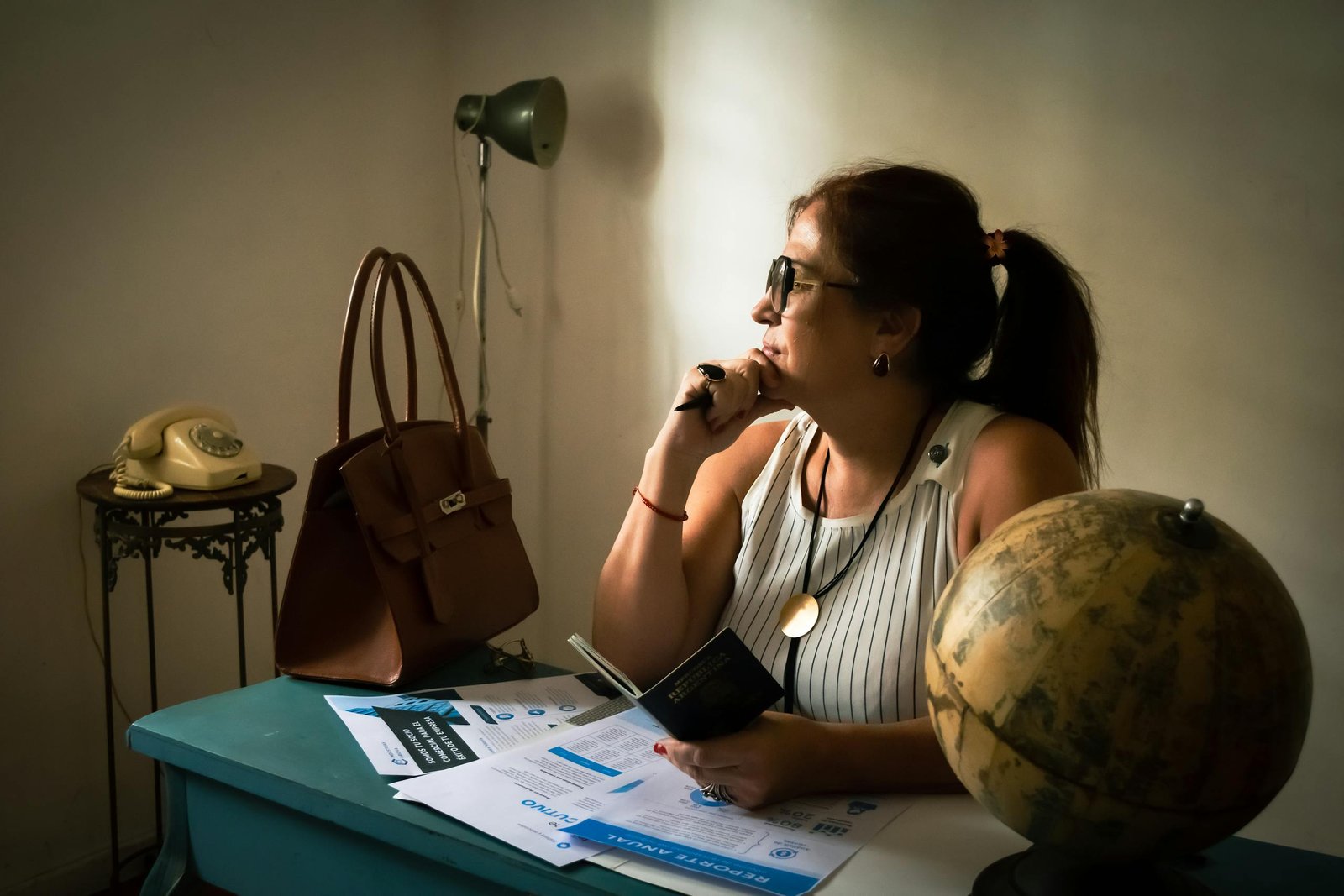 A woman in a vintage office contemplating with a globe and travel documents, seemingly thinking about travel preparation