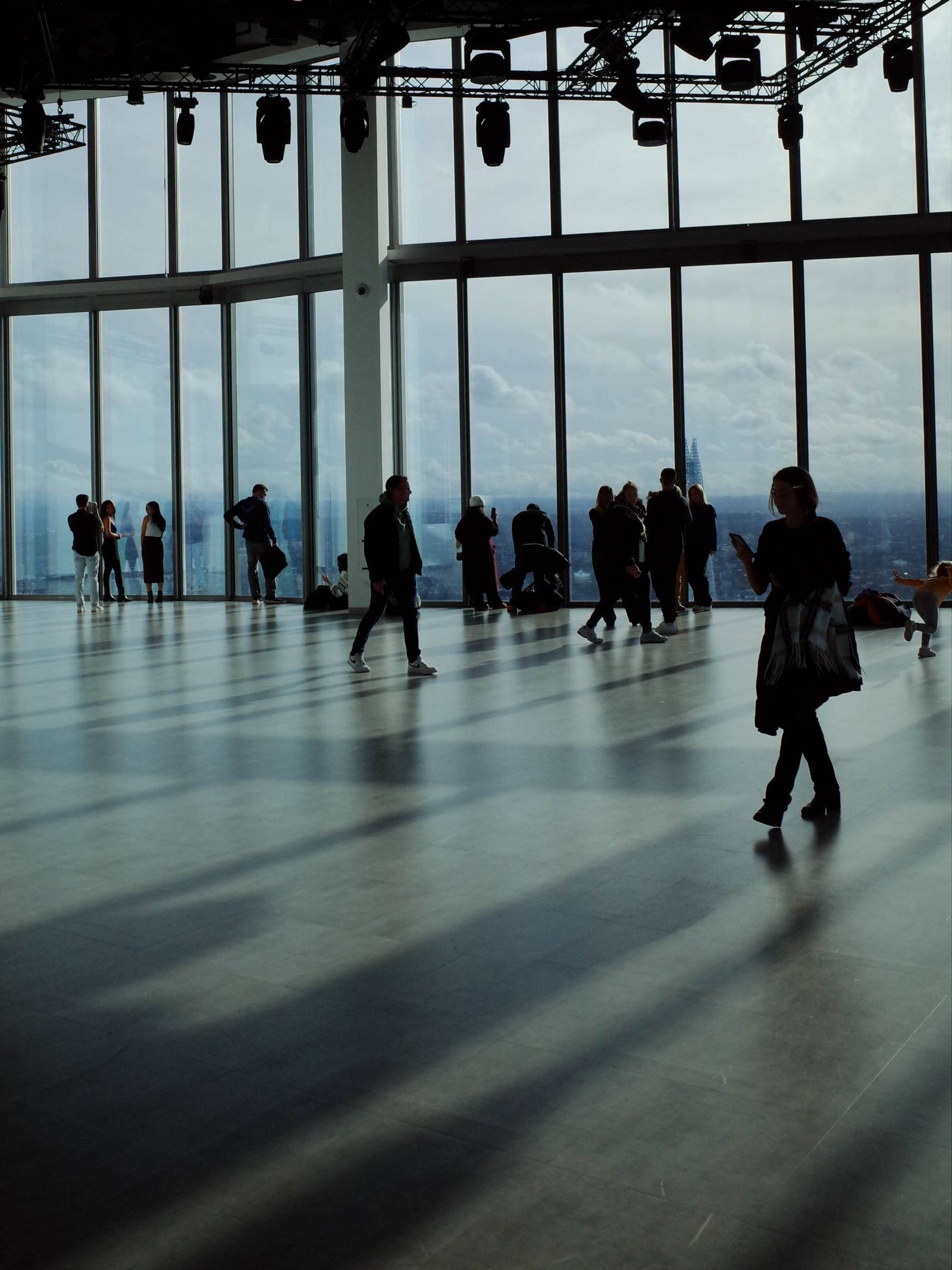 Visitors inside Horizon 22 viewing gallery in London, standing by floor-to-ceiling windows with panoramic skyline views and long shadows cast across the open space.