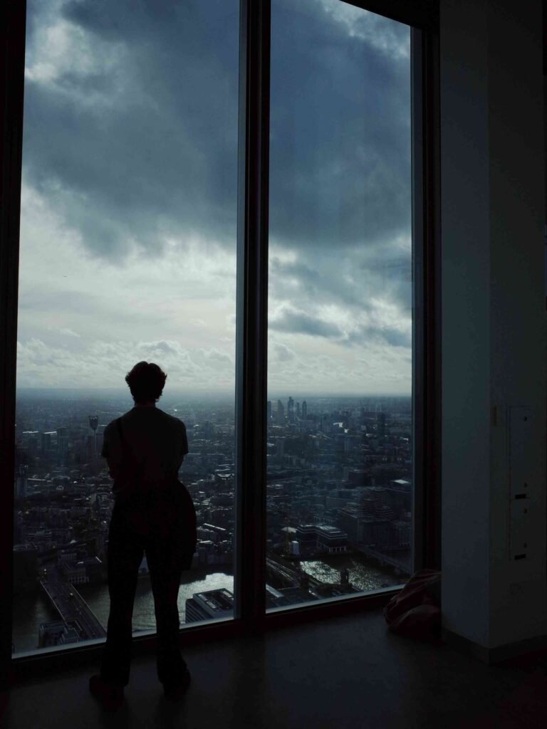 Silhouette of a visitor standing by floor-to-ceiling windows at Horizon 22, looking out over London from above.