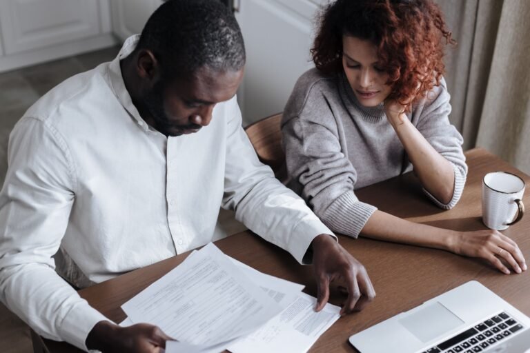 A couple reviews important visa application documents together at a home desk with a laptop.