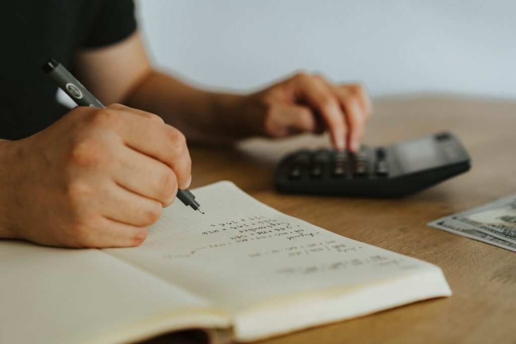 Close-up of hands writing calculations in a notebook with a calculator, focused on budgeting for visa costs